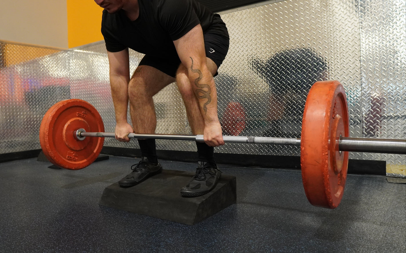 Person lifting a barbell with red weight plates in a gym setting